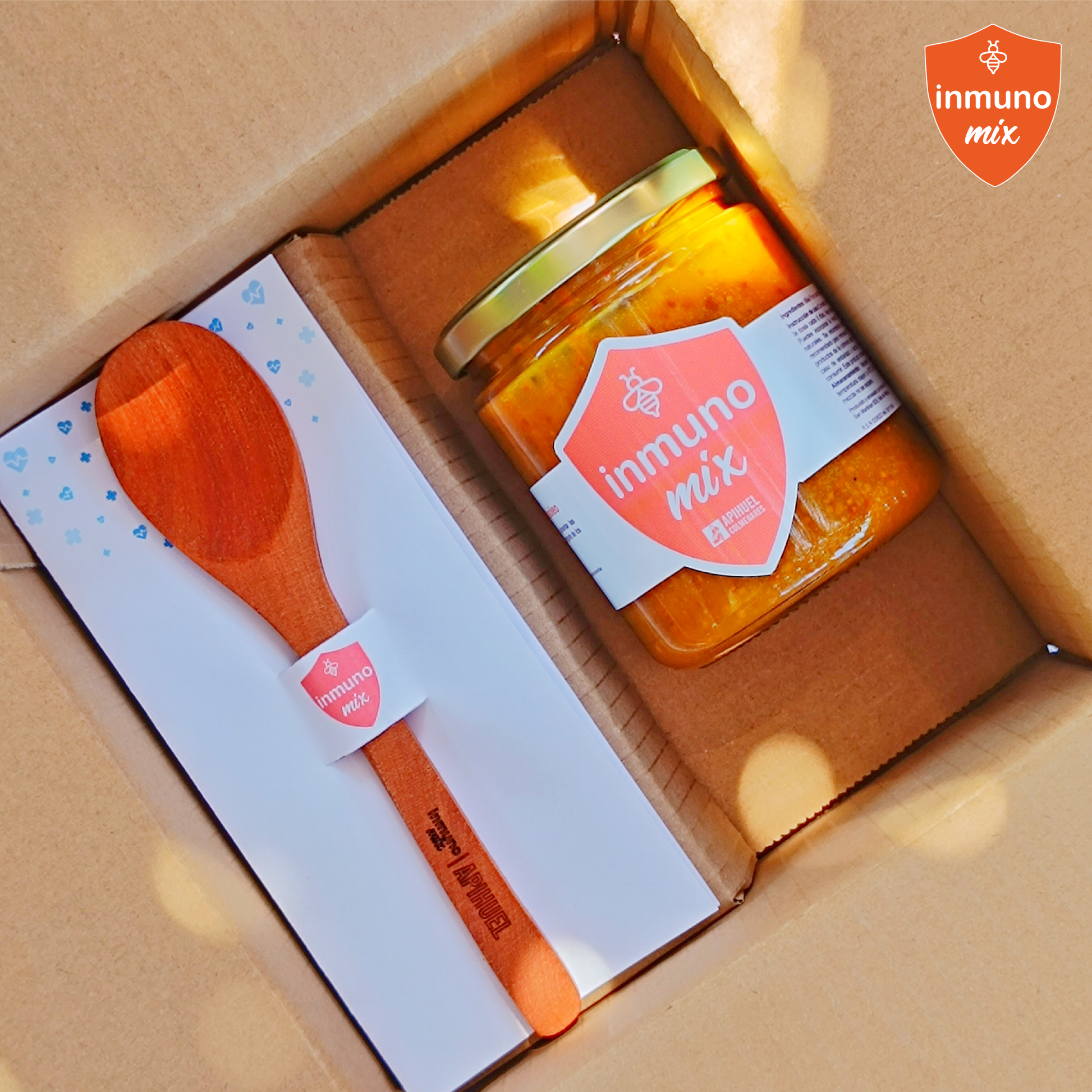 Inmuno Mix jar with orange jam, wooden spoon, and sauce in a box.